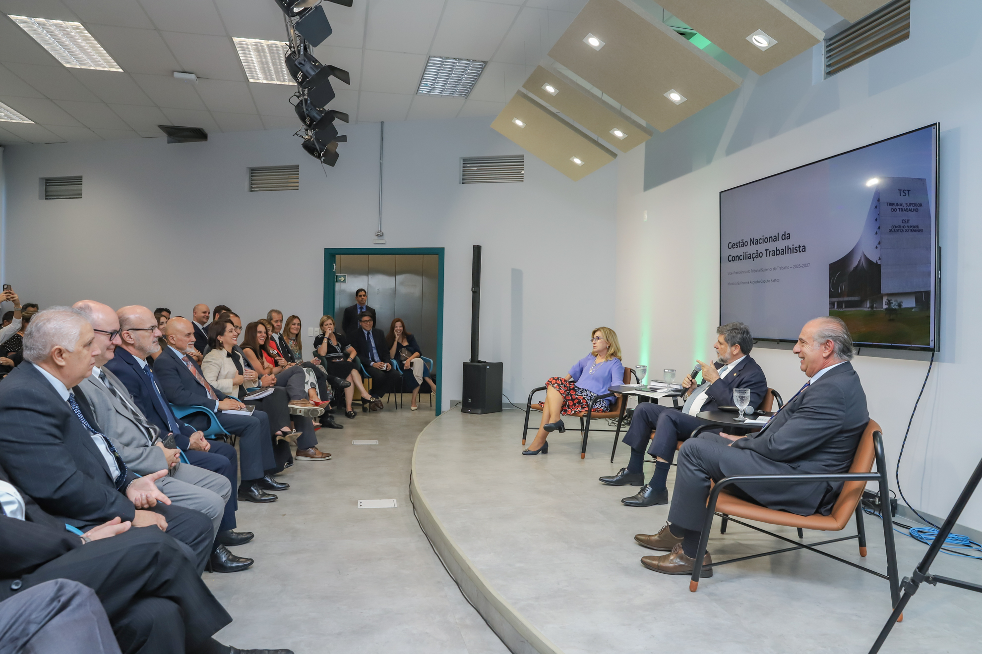 Platéia observa os três magistrados sentados à frente. Ministro fala ao microfone. 