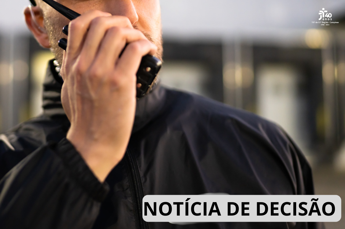 Imagem em close mostra parte do rosto e do tronco de um vigilante uniformizado, utilizando um rádio comunicador junto ao rosto. O fundo está desfocado, sugerindo um ambiente corporativo ou comercial. No canto inferior direito, há a inscrição 
