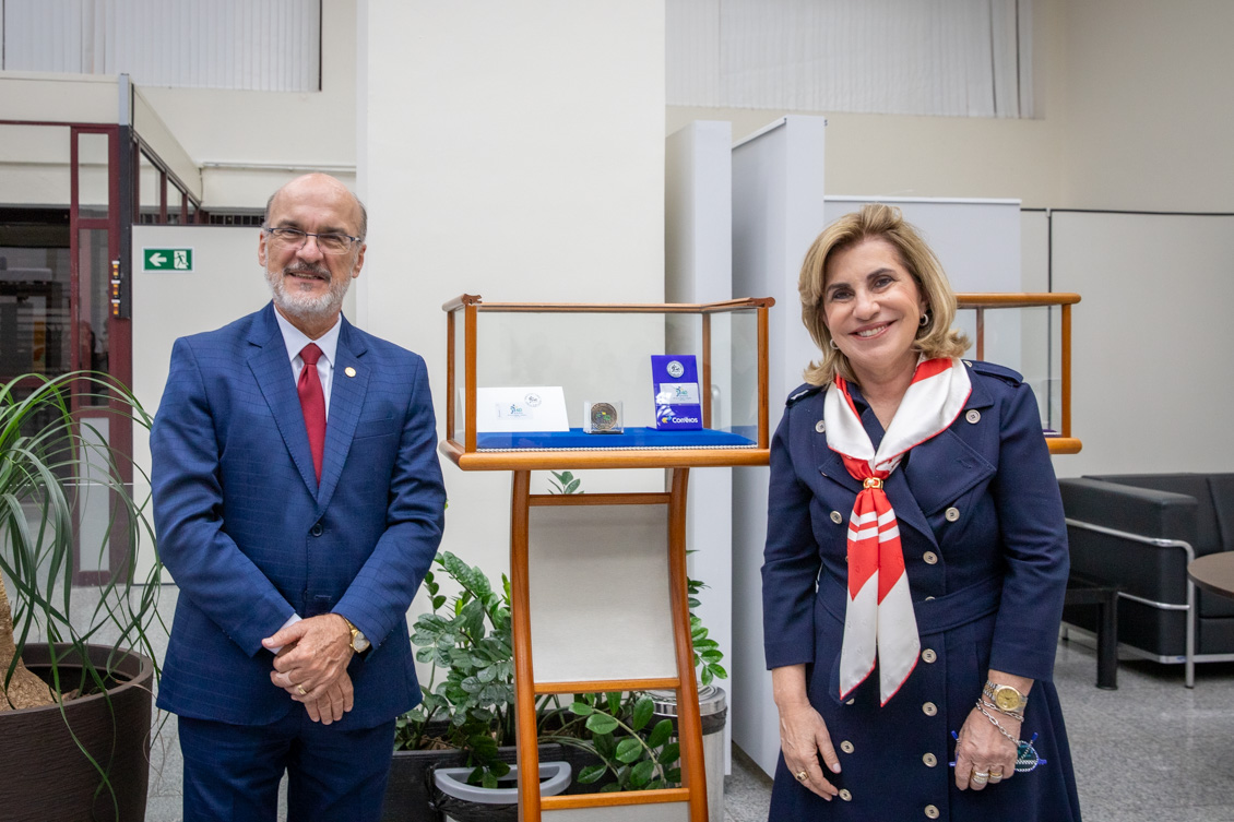 Um homem e uma mulher posam para a foto ao lado de uma caixa onde estão em exposição um selo e uma moeda comemorativa dos 40 anos do TRT 15.